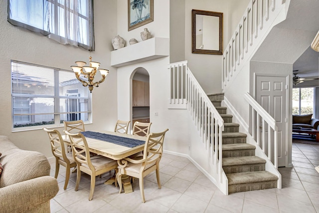 tiled dining area with a towering ceiling and ceiling fan with notable chandelier