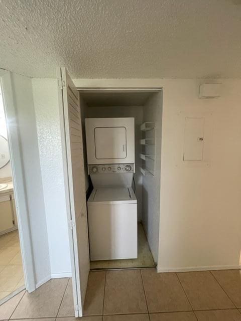 laundry room featuring a textured ceiling, light tile patterned floors, and stacked washing maching and dryer