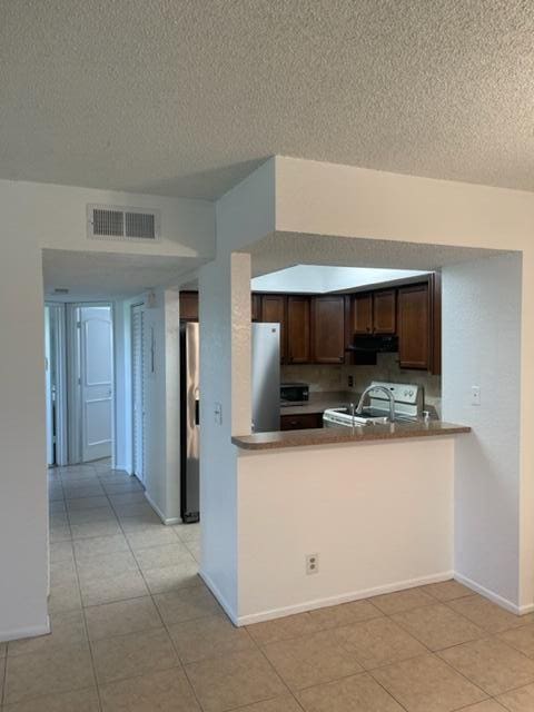 kitchen with stove, kitchen peninsula, a textured ceiling, light tile patterned floors, and stainless steel fridge