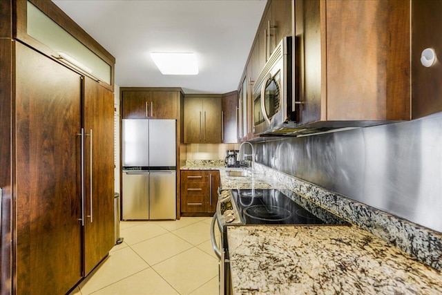 kitchen featuring light stone countertops, light tile patterned floors, appliances with stainless steel finishes, and sink