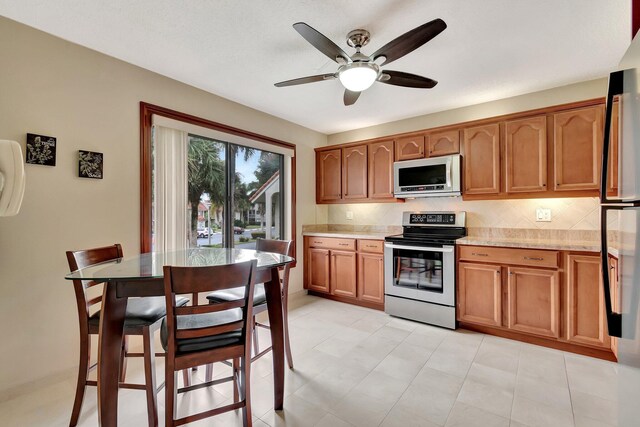 kitchen with ceiling fan, appliances with stainless steel finishes, backsplash, and light stone counters