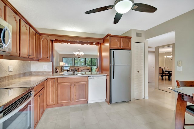 kitchen with pendant lighting, sink, stainless steel appliances, tasteful backsplash, and ceiling fan with notable chandelier