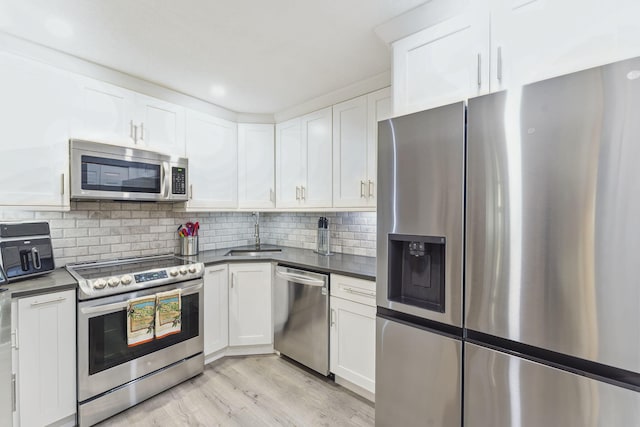 kitchen with sink, white cabinets, backsplash, stainless steel appliances, and light hardwood / wood-style flooring