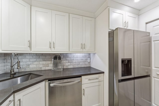 kitchen featuring sink, appliances with stainless steel finishes, white cabinets, decorative backsplash, and dark stone counters