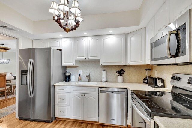 kitchen with an inviting chandelier, white cabinetry, stainless steel appliances, light hardwood / wood-style flooring, and sink