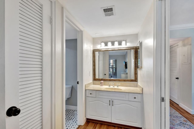 bathroom with toilet, crown molding, hardwood / wood-style flooring, and vanity