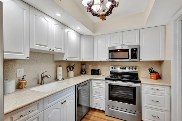 kitchen featuring white cabinetry, stainless steel appliances, an inviting chandelier, sink, and backsplash