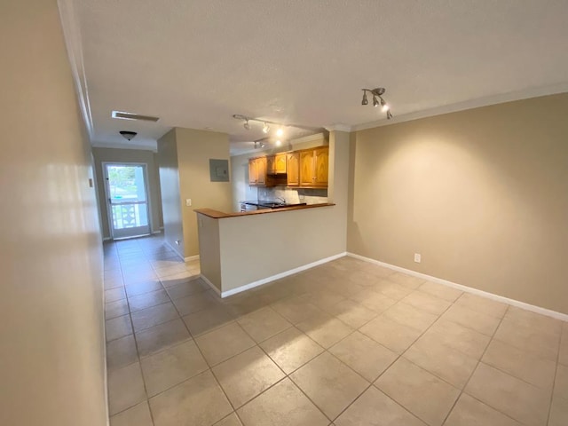 kitchen with kitchen peninsula, a kitchen breakfast bar, light tile patterned flooring, track lighting, and crown molding