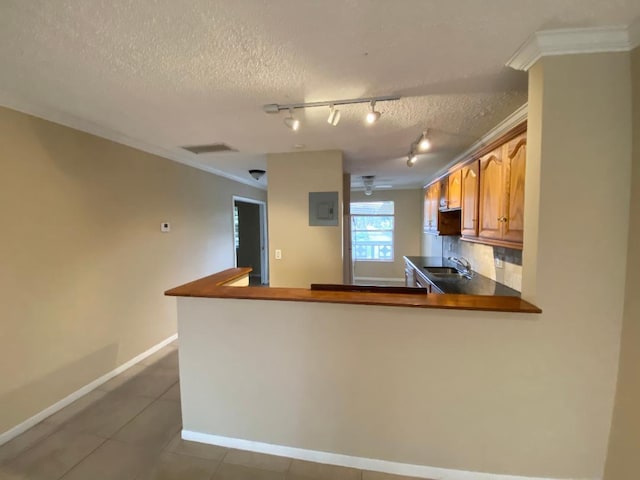 kitchen with tile patterned flooring, backsplash, kitchen peninsula, sink, and crown molding