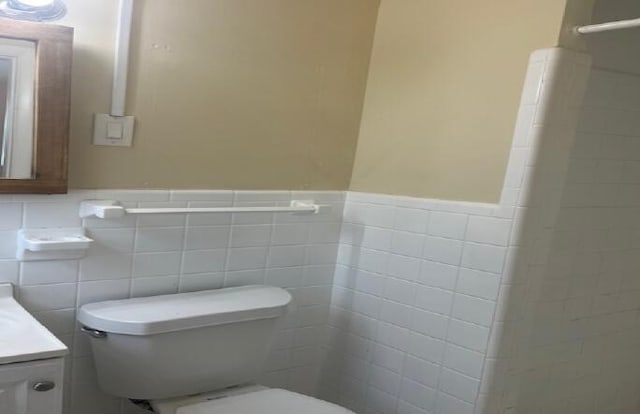 bathroom featuring toilet, tile walls, and vanity