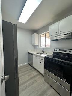 kitchen featuring white cabinetry, stainless steel appliances, a skylight, light hardwood / wood-style floors, and sink