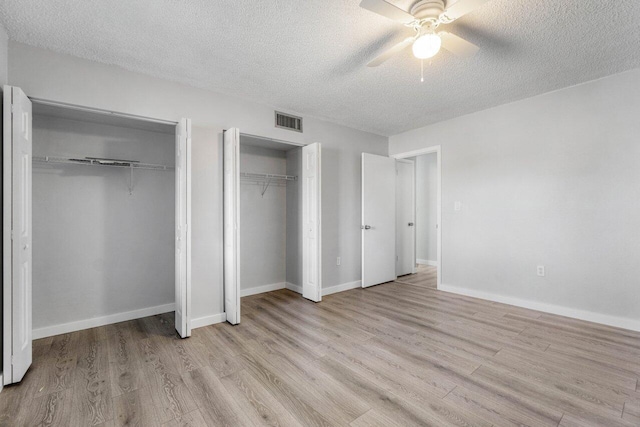 unfurnished bedroom featuring ceiling fan, two closets, light hardwood / wood-style floors, and a textured ceiling