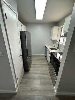 kitchen with sink, white cabinetry, black fridge, and stainless steel electric range