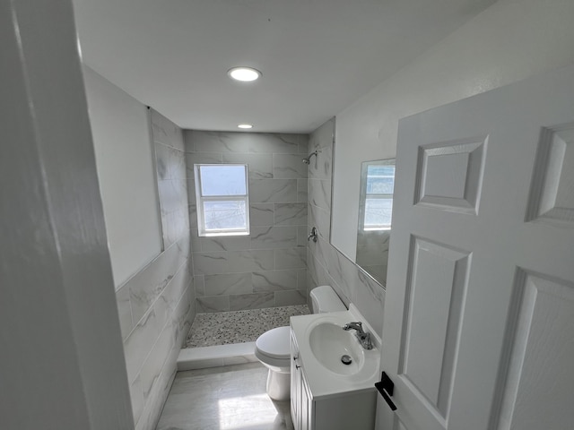 bathroom with plenty of natural light, tiled shower, vanity, and toilet