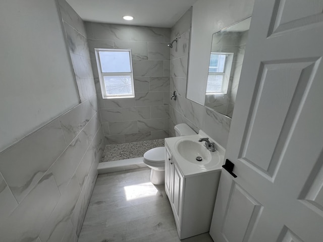 bathroom with tile walls, tiled shower, vanity, and toilet