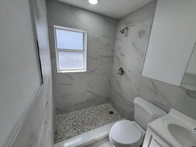 bathroom featuring tile walls, toilet, tiled shower, and vanity