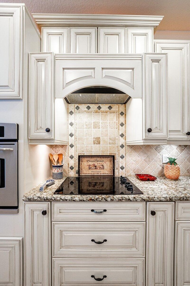 kitchen featuring white cabinetry, oven, decorative backsplash, light stone counters, and black electric cooktop