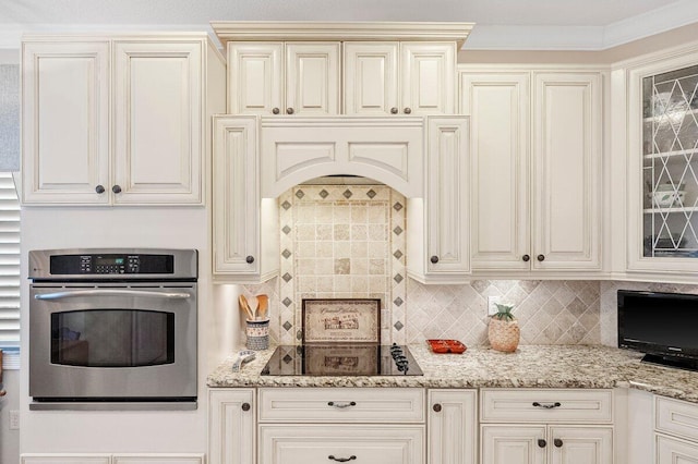 kitchen featuring crown molding, backsplash, light stone counters, black electric stovetop, and oven