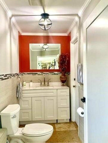 bathroom with toilet, ornamental molding, tile walls, and vanity