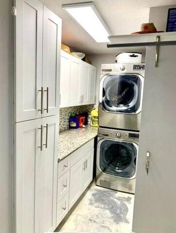 laundry area with cabinets and stacked washer and clothes dryer