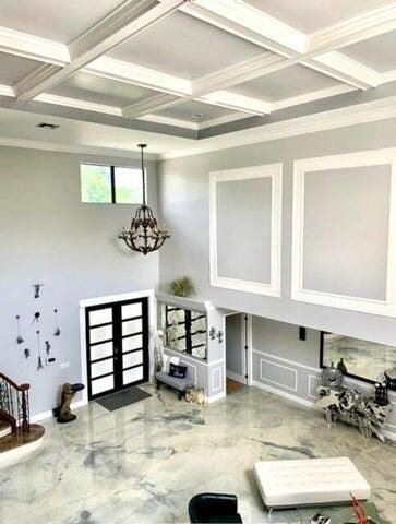 entrance foyer with crown molding, beam ceiling, coffered ceiling, and a notable chandelier