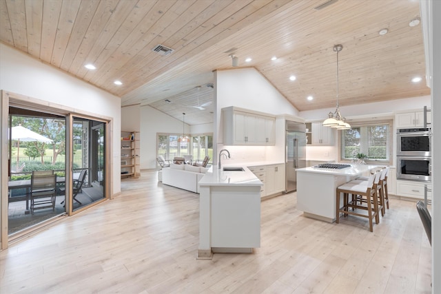 kitchen featuring hanging light fixtures, stainless steel appliances, light countertops, light wood-type flooring, and white cabinetry