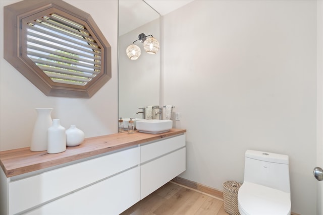 bathroom with toilet, wood finished floors, vanity, and baseboards