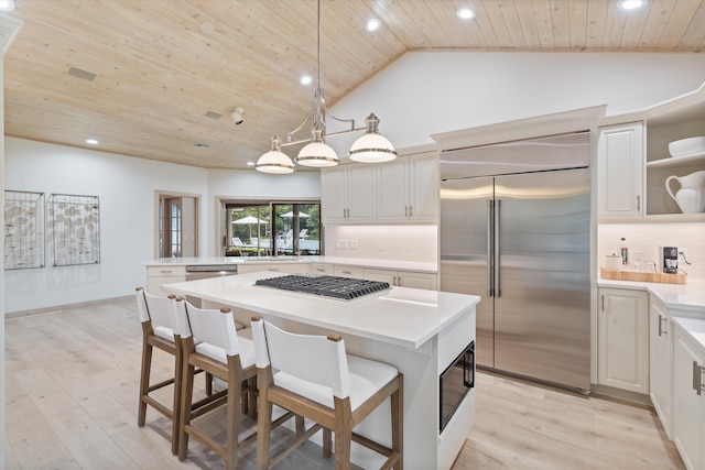 kitchen with light countertops, appliances with stainless steel finishes, open shelves, a kitchen bar, and pendant lighting