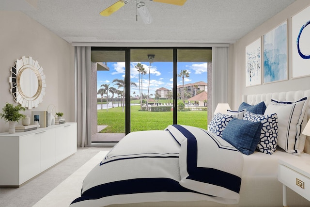 carpeted bedroom with ceiling fan, access to outside, a textured ceiling, and a wall of windows