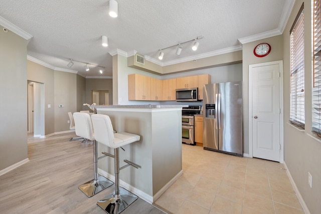 kitchen featuring appliances with stainless steel finishes, light brown cabinets, a kitchen breakfast bar, a textured ceiling, and crown molding