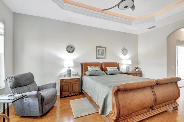 bedroom featuring arched walkways, a tray ceiling, visible vents, light wood-style floors, and ornamental molding