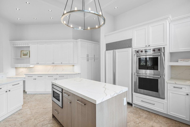 kitchen with a high ceiling, white cabinets, a center island, built in appliances, and light stone counters