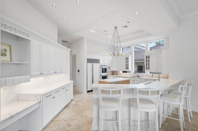 kitchen with pendant lighting, white cabinets, a tray ceiling, and sink