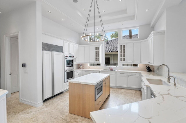 kitchen featuring built in appliances, a kitchen island, pendant lighting, white cabinets, and sink