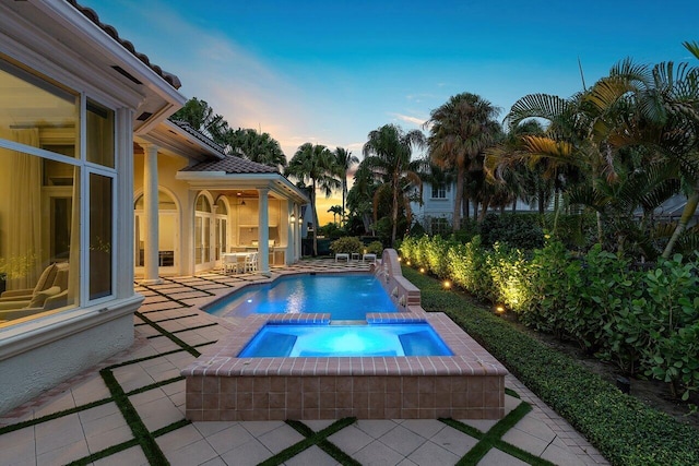 pool at dusk with pool water feature, a patio, and an in ground hot tub