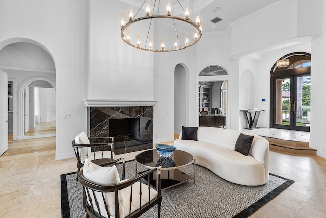 living room featuring an inviting chandelier, a towering ceiling, ornamental molding, french doors, and a high end fireplace