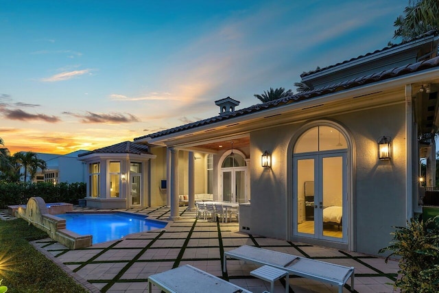 back house at dusk with a swimming pool with hot tub, french doors, and a patio area