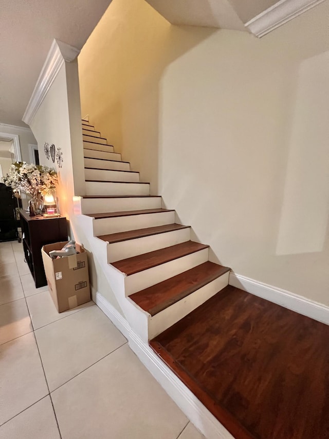 stairway with tile patterned floors and ornamental molding