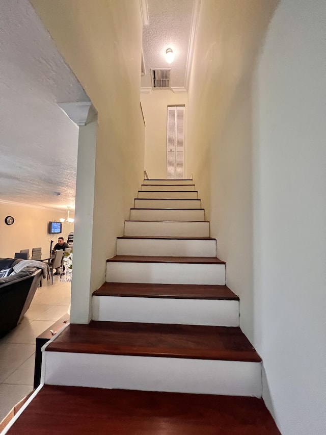 stairway with a textured ceiling and ornamental molding