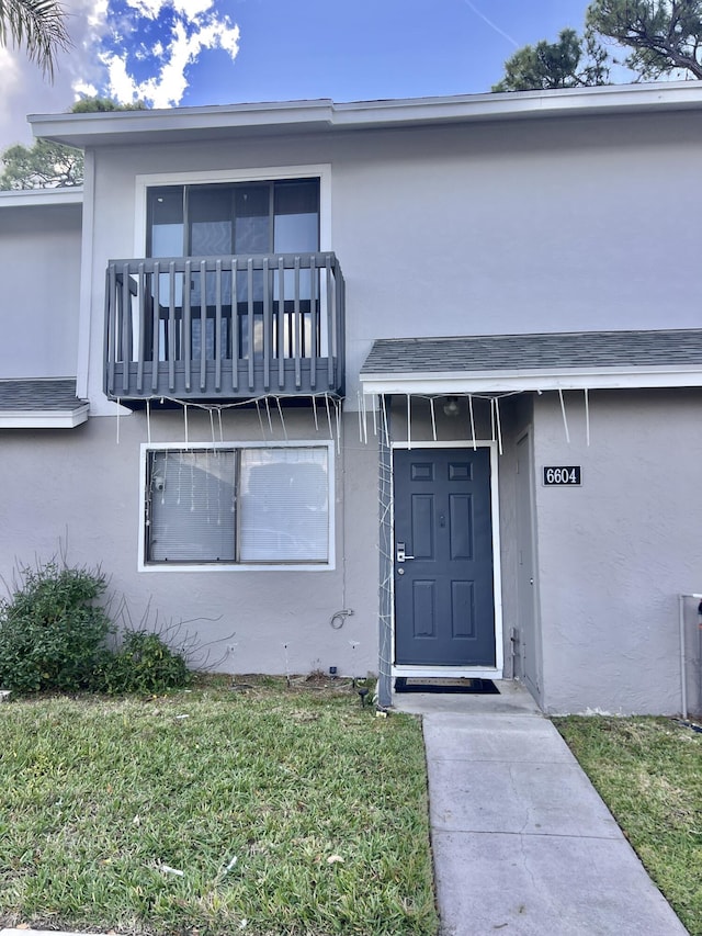 view of exterior entry featuring a lawn and a balcony