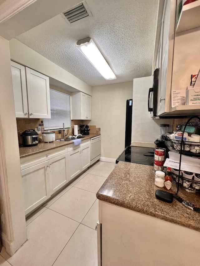 kitchen with sink, light tile patterned floors, white dishwasher, a textured ceiling, and white cabinets