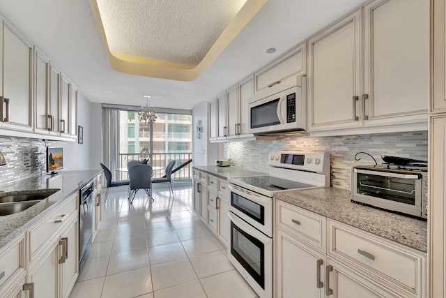 kitchen featuring sink, tasteful backsplash, light tile patterned floors, a tray ceiling, and white appliances