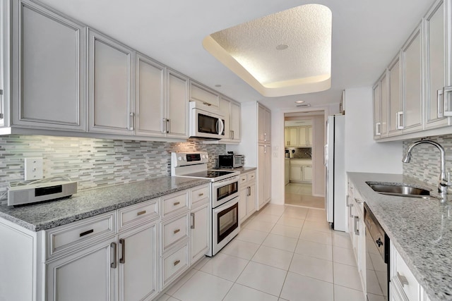 kitchen with sink, light stone counters, backsplash, and white appliances