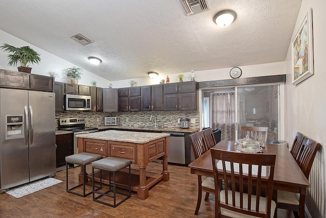 kitchen featuring tasteful backsplash, a center island, dark brown cabinetry, dark wood-type flooring, and appliances with stainless steel finishes