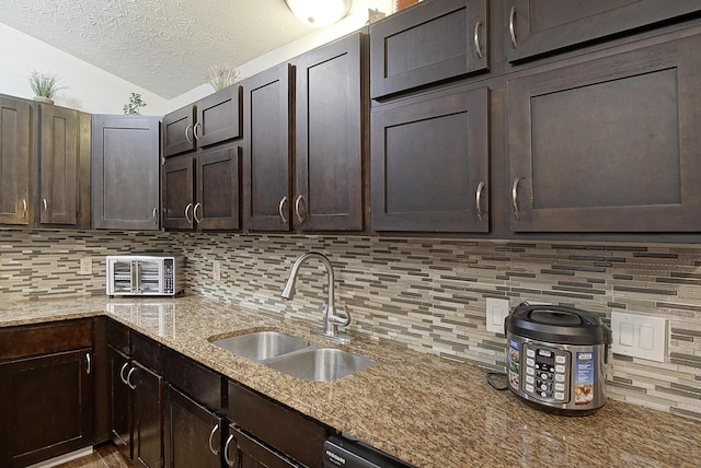 kitchen with light stone countertops, a textured ceiling, dark brown cabinetry, decorative backsplash, and sink