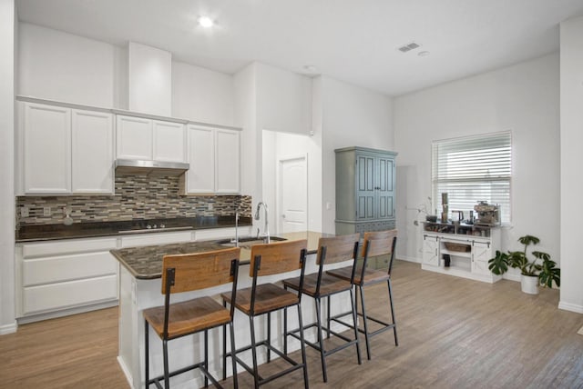 kitchen with a sink, visible vents, white cabinets, light wood finished floors, and dark countertops