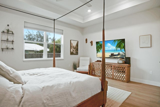 bedroom with ornamental molding, a tray ceiling, and light hardwood / wood-style flooring