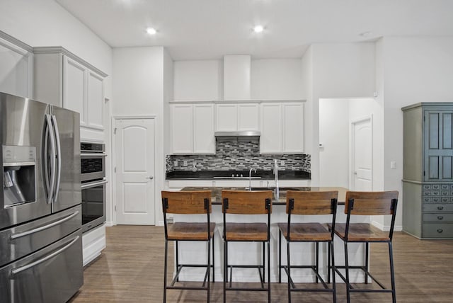 kitchen with a kitchen bar, dark wood-style flooring, stainless steel appliances, and decorative backsplash