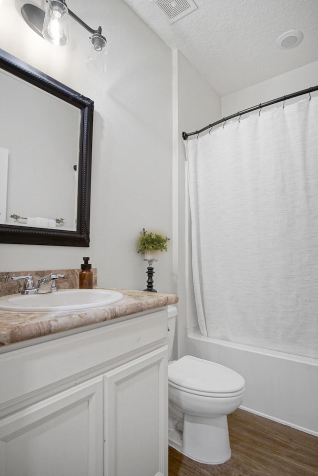 full bathroom with hardwood / wood-style floors, vanity, toilet, shower / bath combo, and a textured ceiling