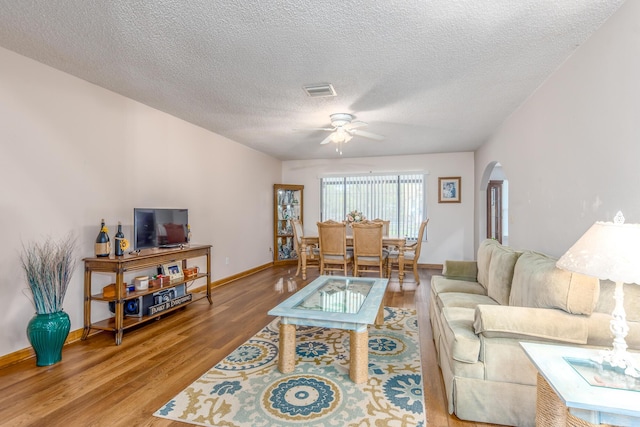 living room featuring wood-type flooring, a textured ceiling, and ceiling fan